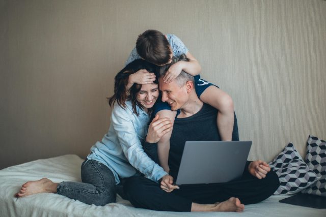 Young family mother, father and child laughing together with laptop